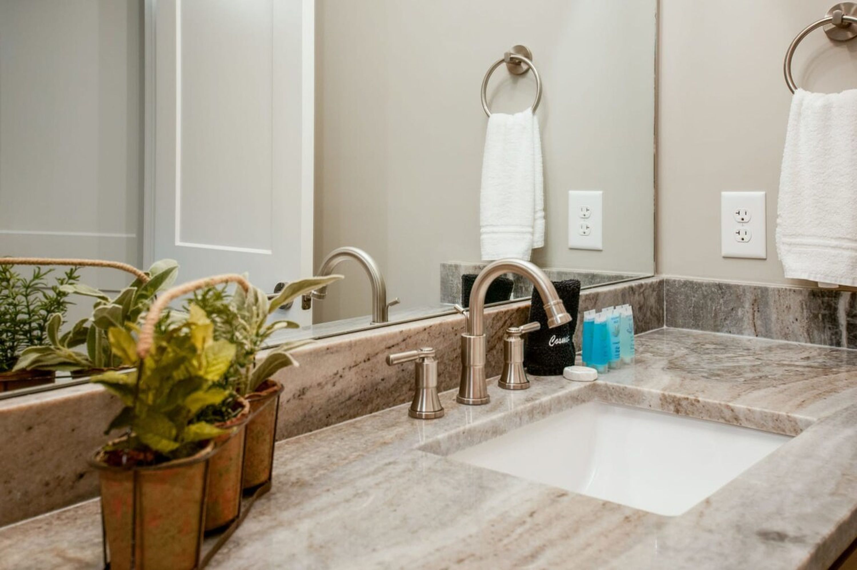 A bathroom with a marble sink, two faucets, a mirror, and a towel rack.