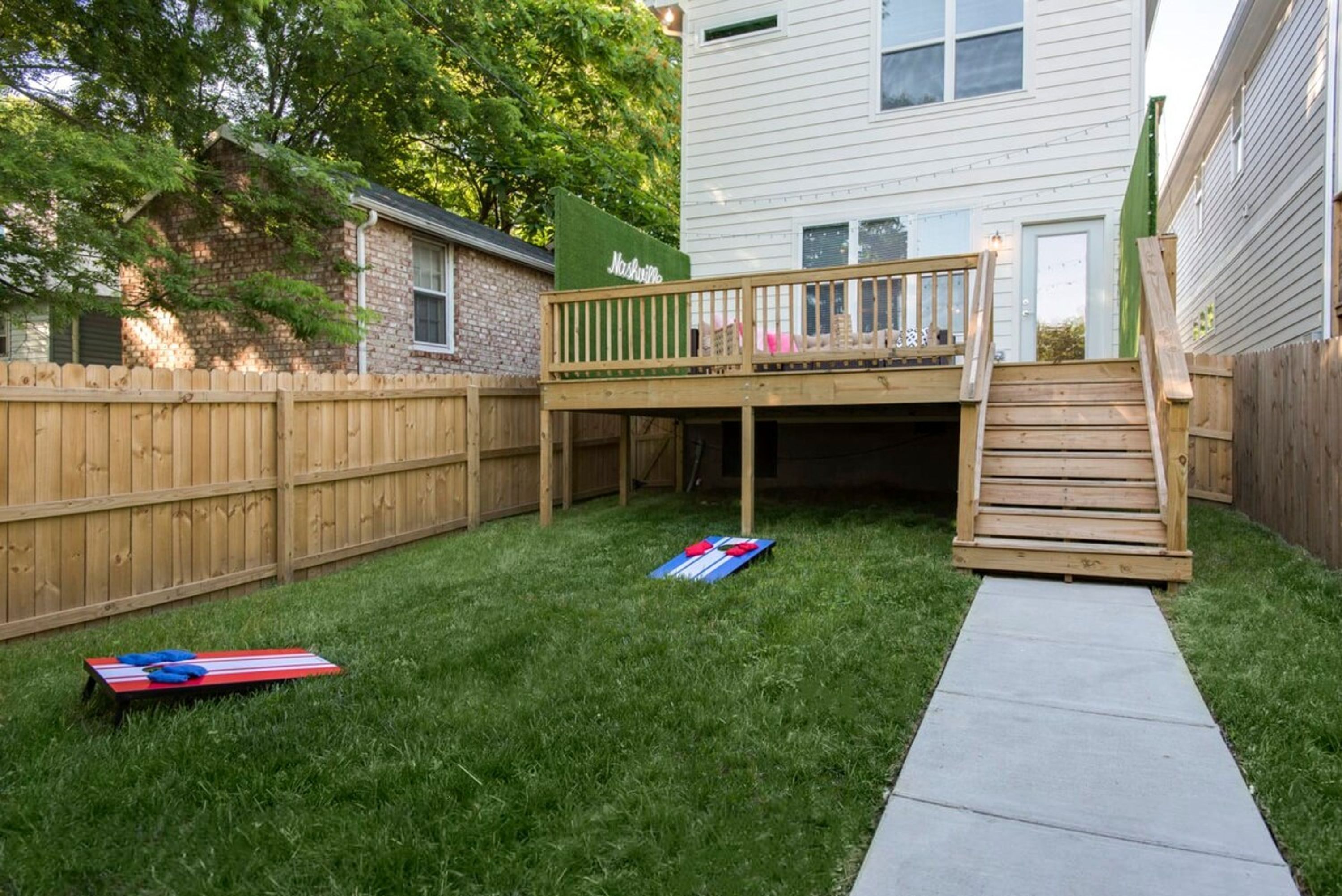 A backyard with a wooden deck, a concrete pathway, and a small play area with a slide.