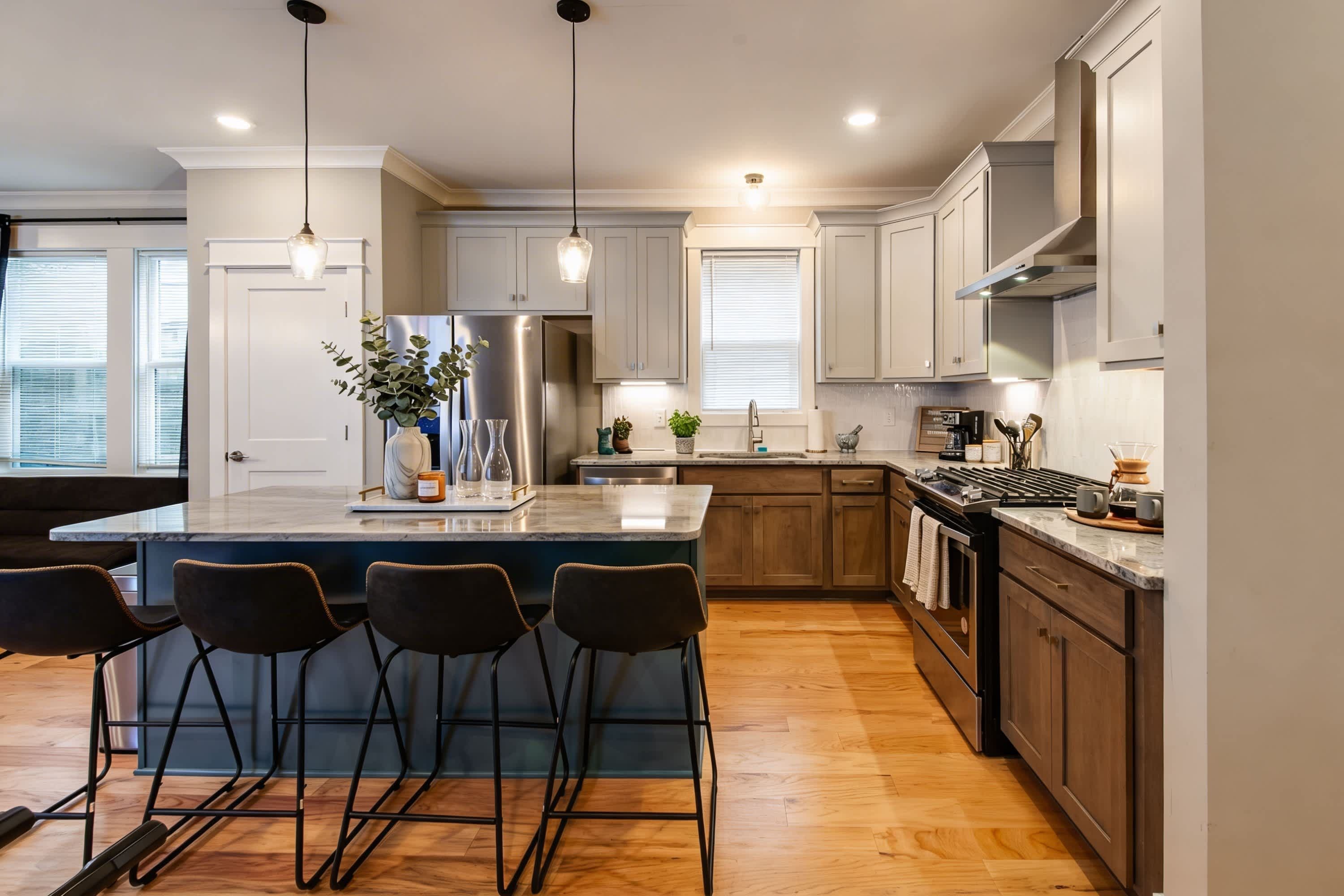 A modern kitchen with a central island, bar stools, stainless steel appliances, and wooden cabinets.