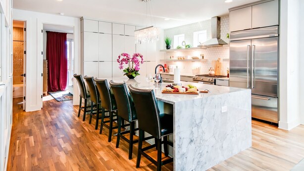 A modern kitchen with a marble island, stainless steel appliances, and a wooden floor.