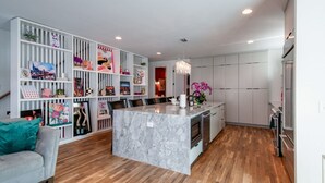 A modern kitchen with a marble island, white cabinetry, and a dining area with a grey sofa.