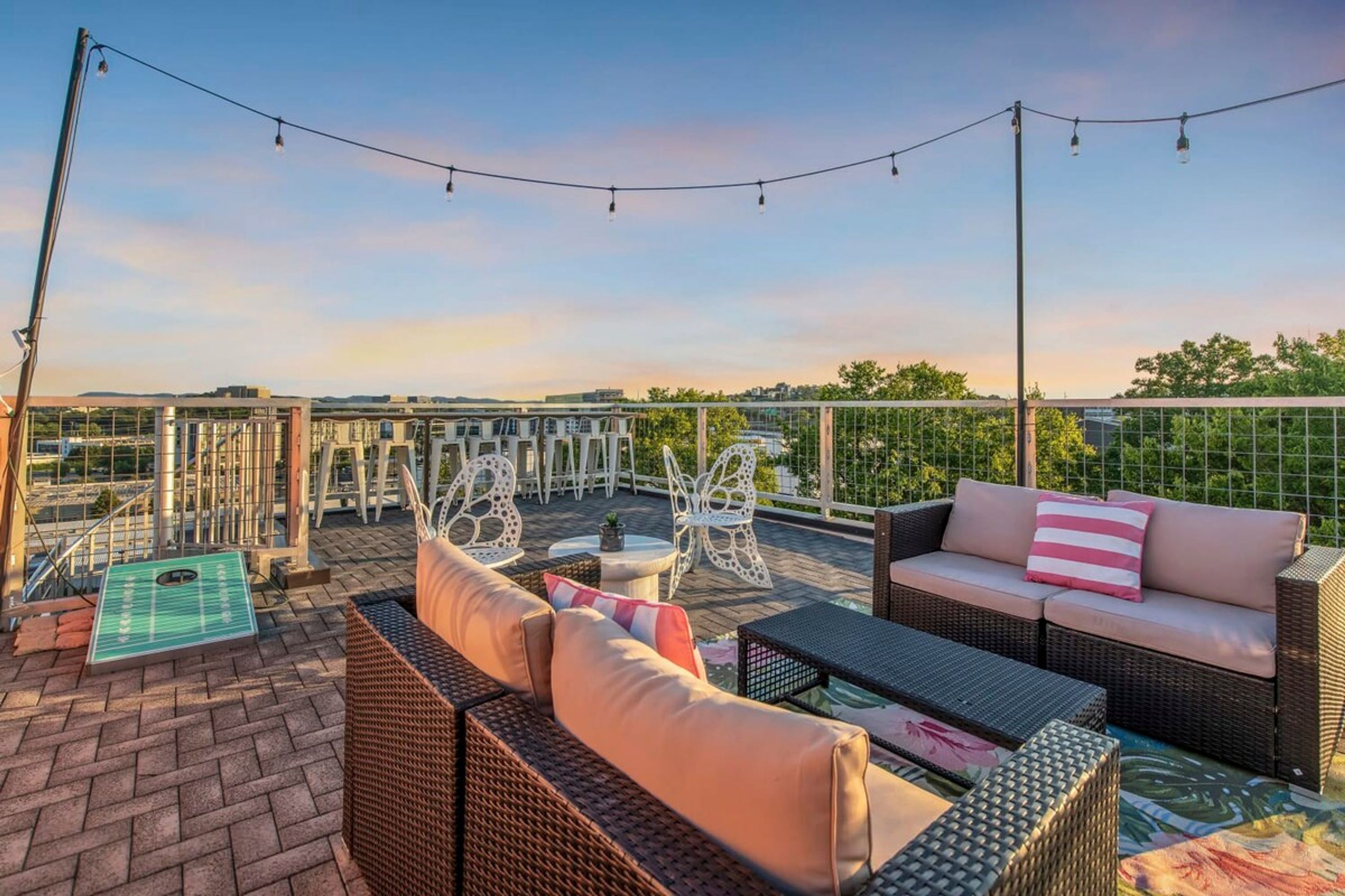 A rooftop patio with wicker furniture, a string of lights, and a view of the cityscape.