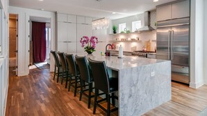 A modern kitchen with a marble island, stainless steel appliances, and a chandelier.