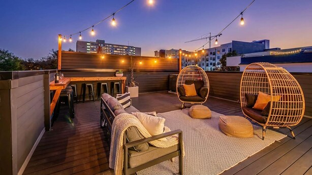 A rooftop terrace with wooden flooring, a bar area, and seating including a hanging chair and cushioned benches. - Close to the Gulch - Book Today (Nashville)