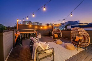 Eine Dachterrasse mit Holzboden, einer Bar und Sitzgelegenheiten, darunter ein Hängesessel und gepolsterte Bänke.
