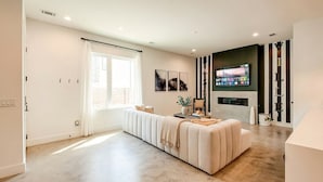 A modern living room with a large sofa, a flat-screen TV mounted on the wall, and a large window with curtains. - Close to the Gulch - Book Today (Nashville)