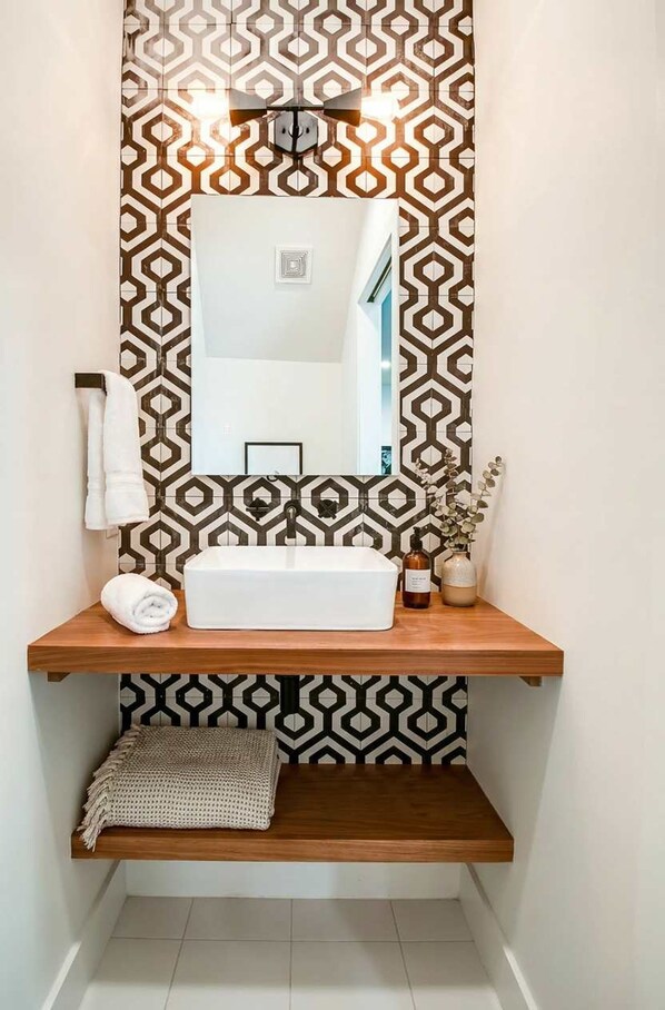 A bathroom with a geometric patterned wall, a white sink, and a mirror above it.