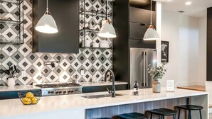 A modern kitchen with a central island, stainless steel appliances, pendant lighting, and a patterned backsplash. - Close to the Gulch - Book Today (Nashville)