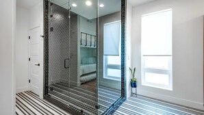 A modern bathroom with a glass-enclosed shower, a white door, a large window, and a striped floor. - Close to the Gulch - Book Today (Nashville)