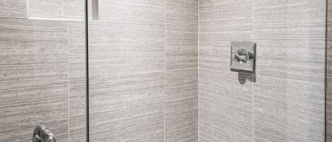 A modern shower with a glass door, a handheld showerhead, and a wall-mounted control panel.