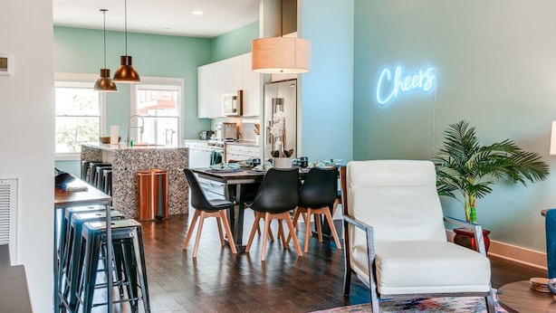 A modern kitchen with a neon sign, a dining area with chairs, and a bar with stools. - Game Room and Skydeck - Book Today (Nashville)