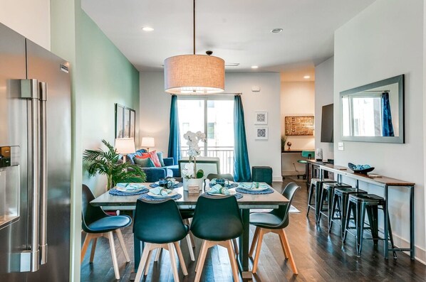 A modern kitchen with a dining area, featuring a large table, chairs, and a hanging light fixture.
