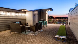 A rooftop patio with outdoor furniture, a small table, and a grassy area. - Game Room and Skydeck - Book Today (Nashville)