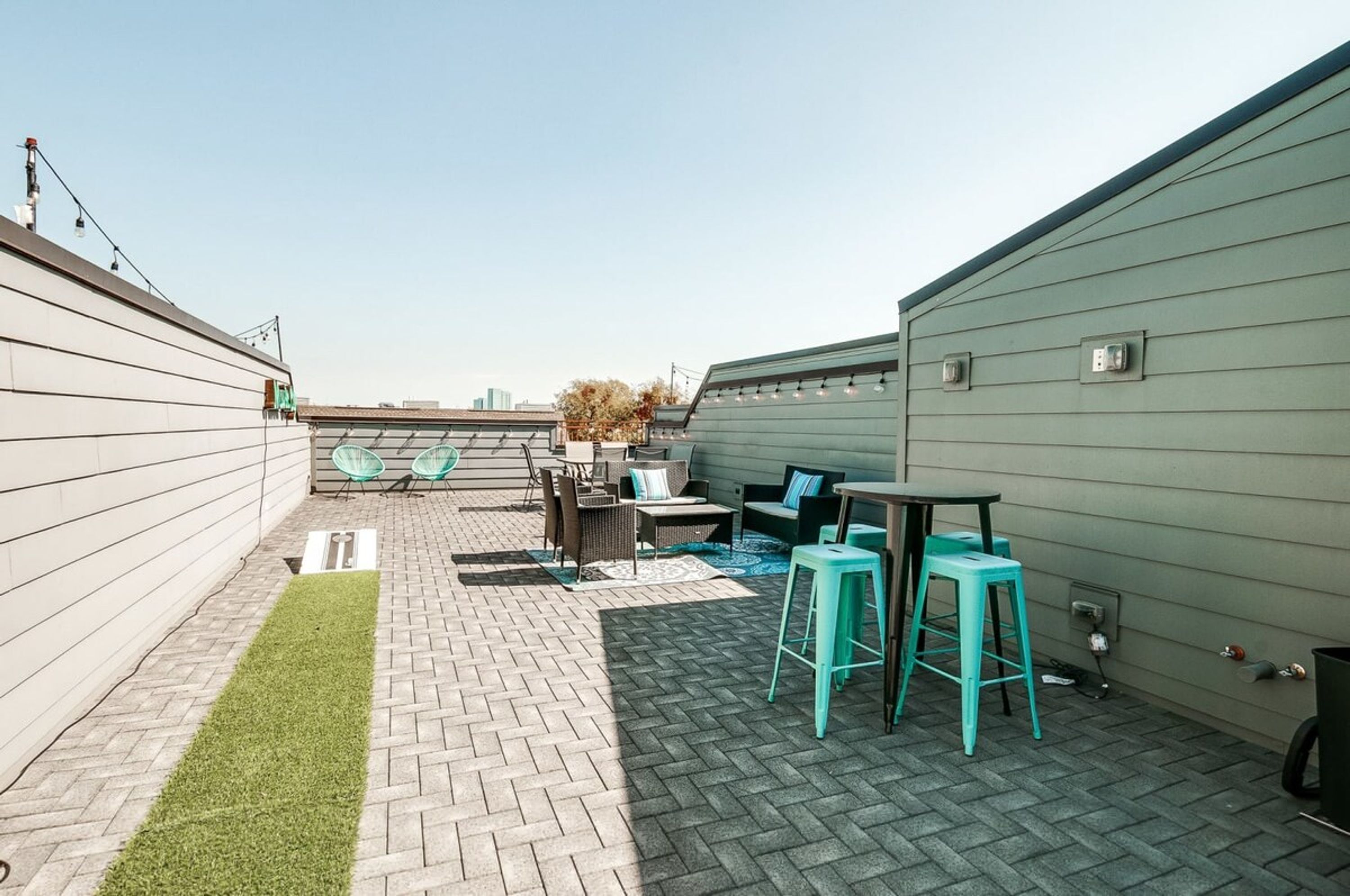A rooftop patio with a brick floor, outdoor furniture, and a small grassy area.