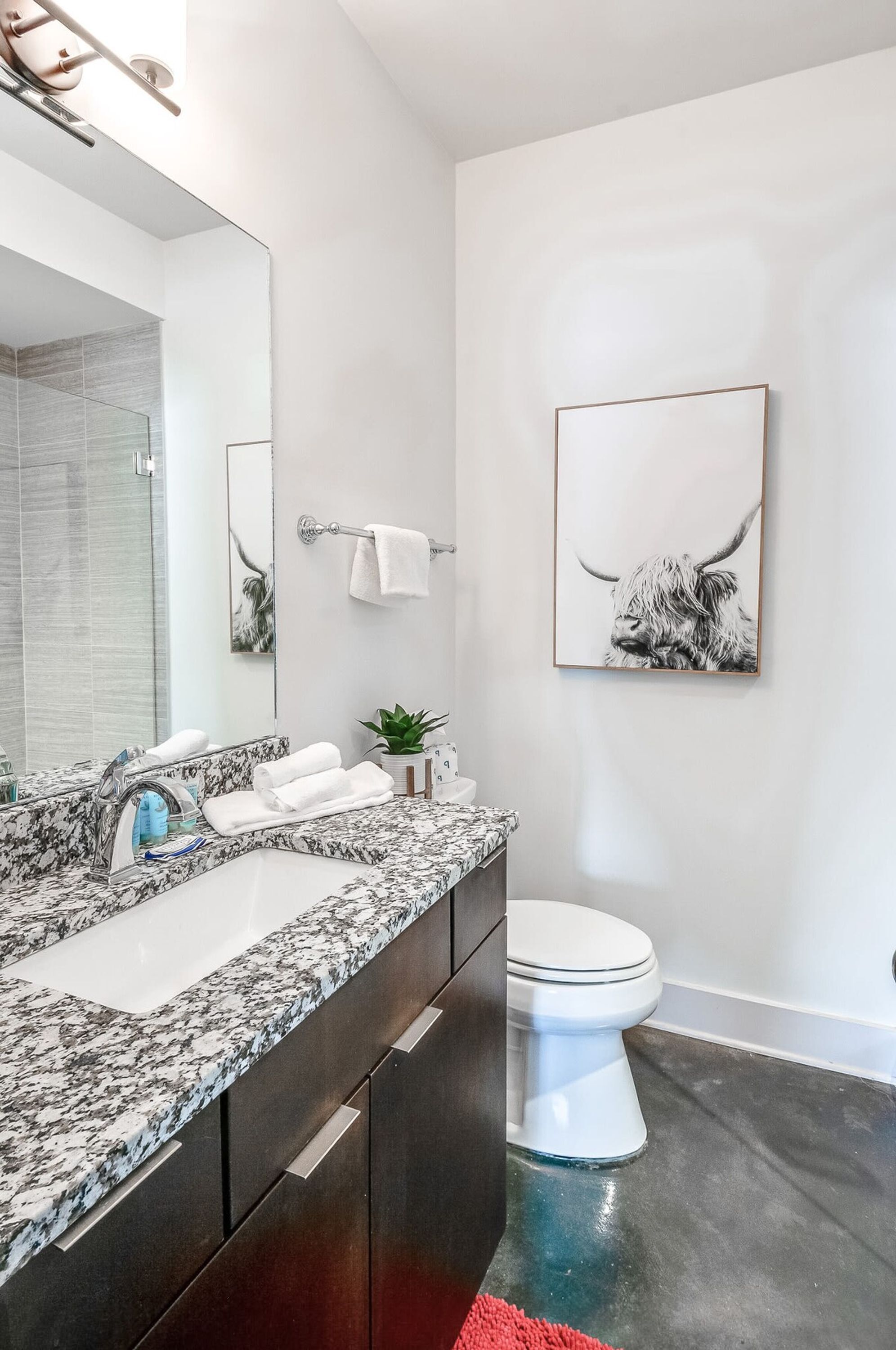A modern bathroom with a granite countertop, a white toilet, and a large mirror.