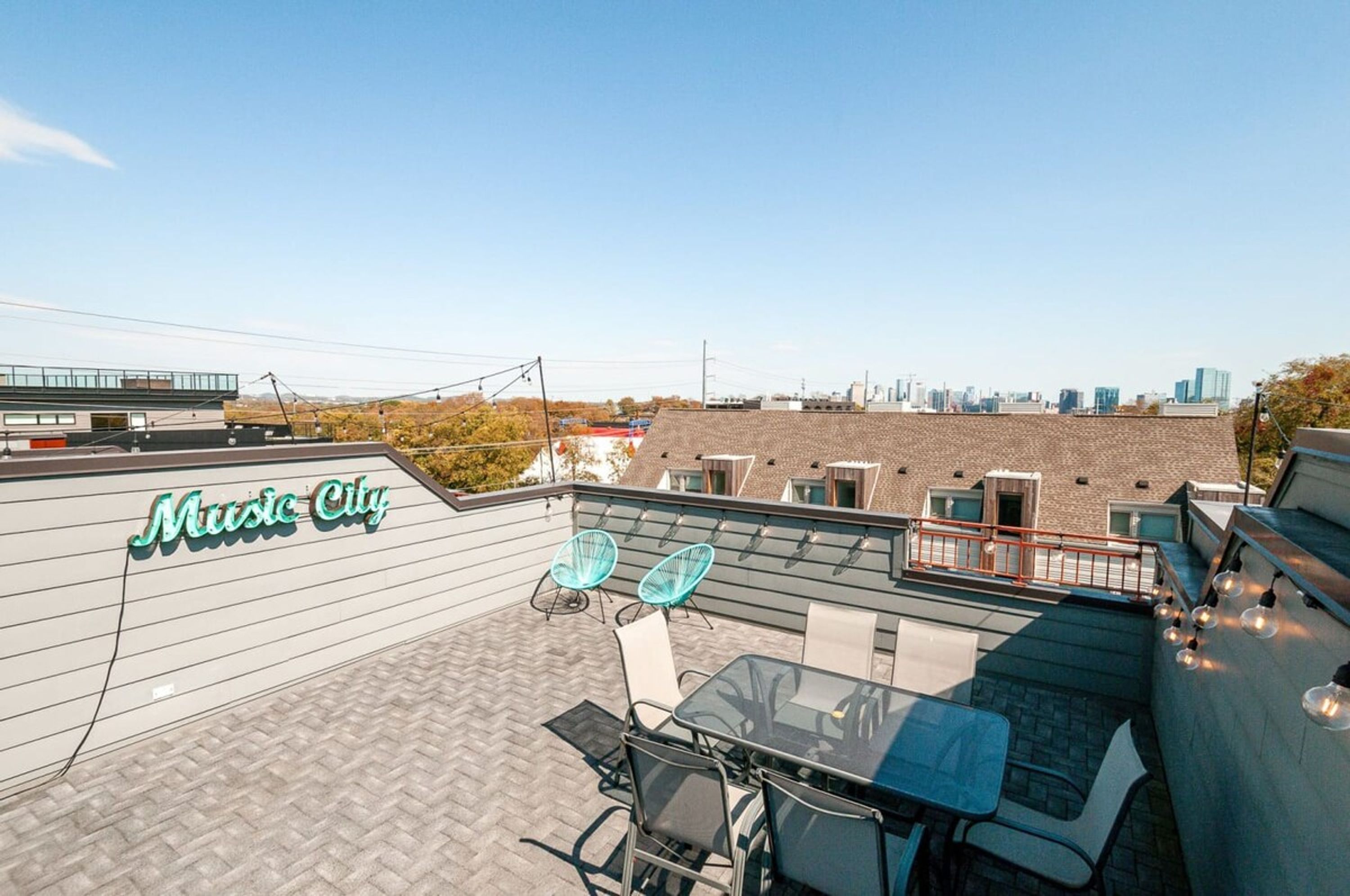 A rooftop terrace with a glass table and chairs, a sign reading "Music City," and a city skyline in the background.