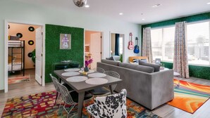 Uma sala de estar moderna com um sofá cinzento, uma mesa de jantar com cadeiras e uma parede verde.