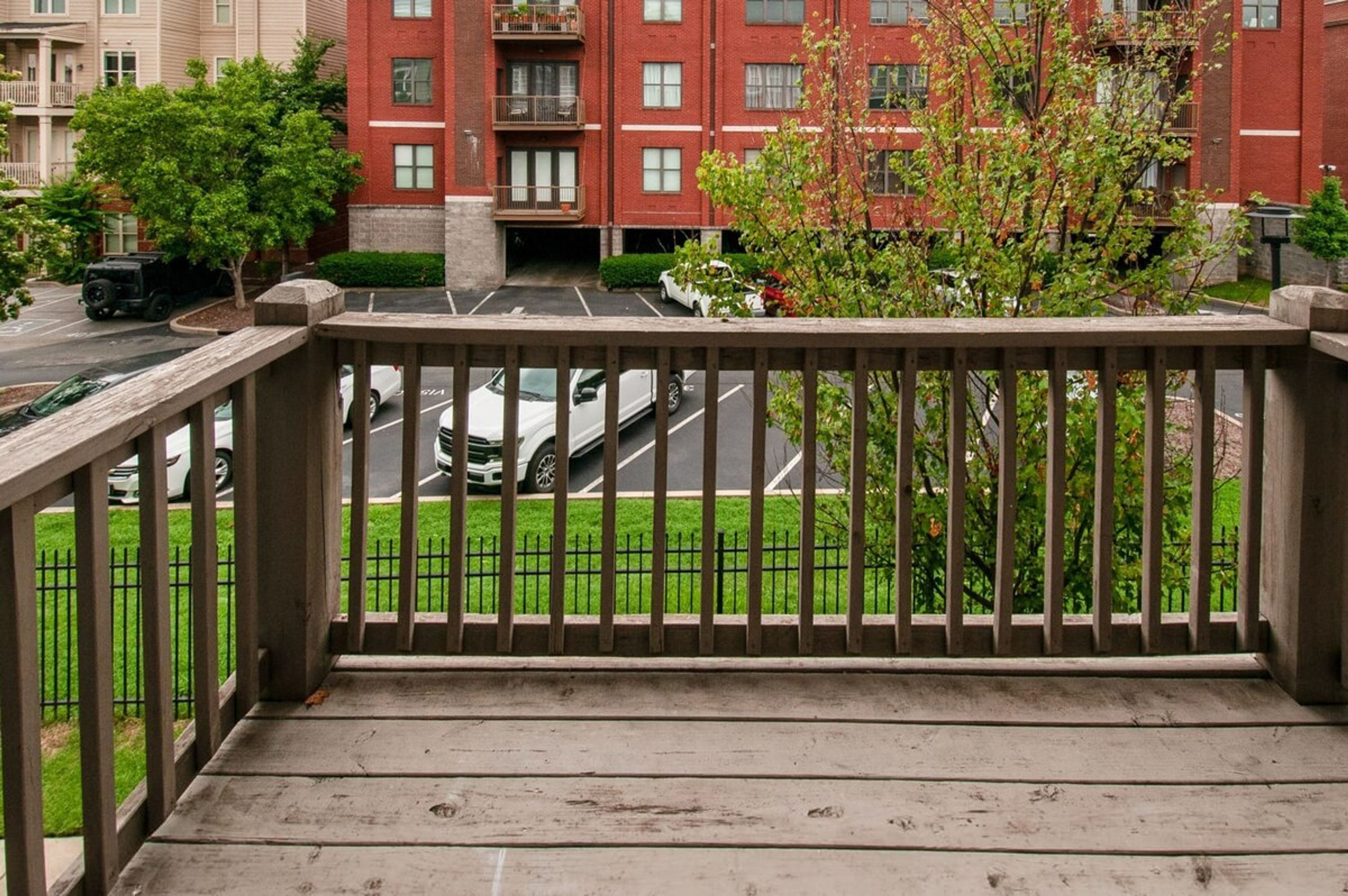 A wooden deck with a view of a parking lot and a red brick building with balconies.