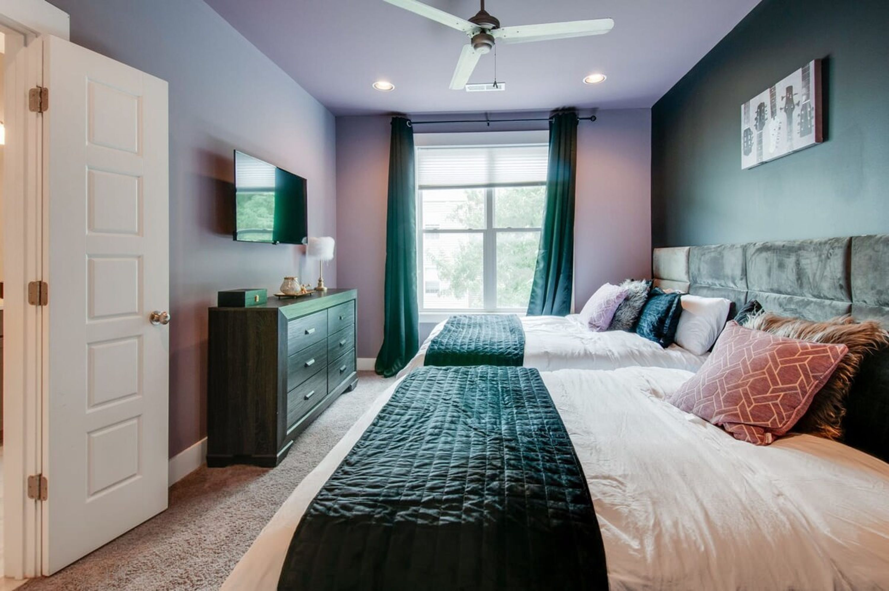 Une chambre à coucher avec un lit, une commode, un téléviseur et une fenêtre avec des rideaux.