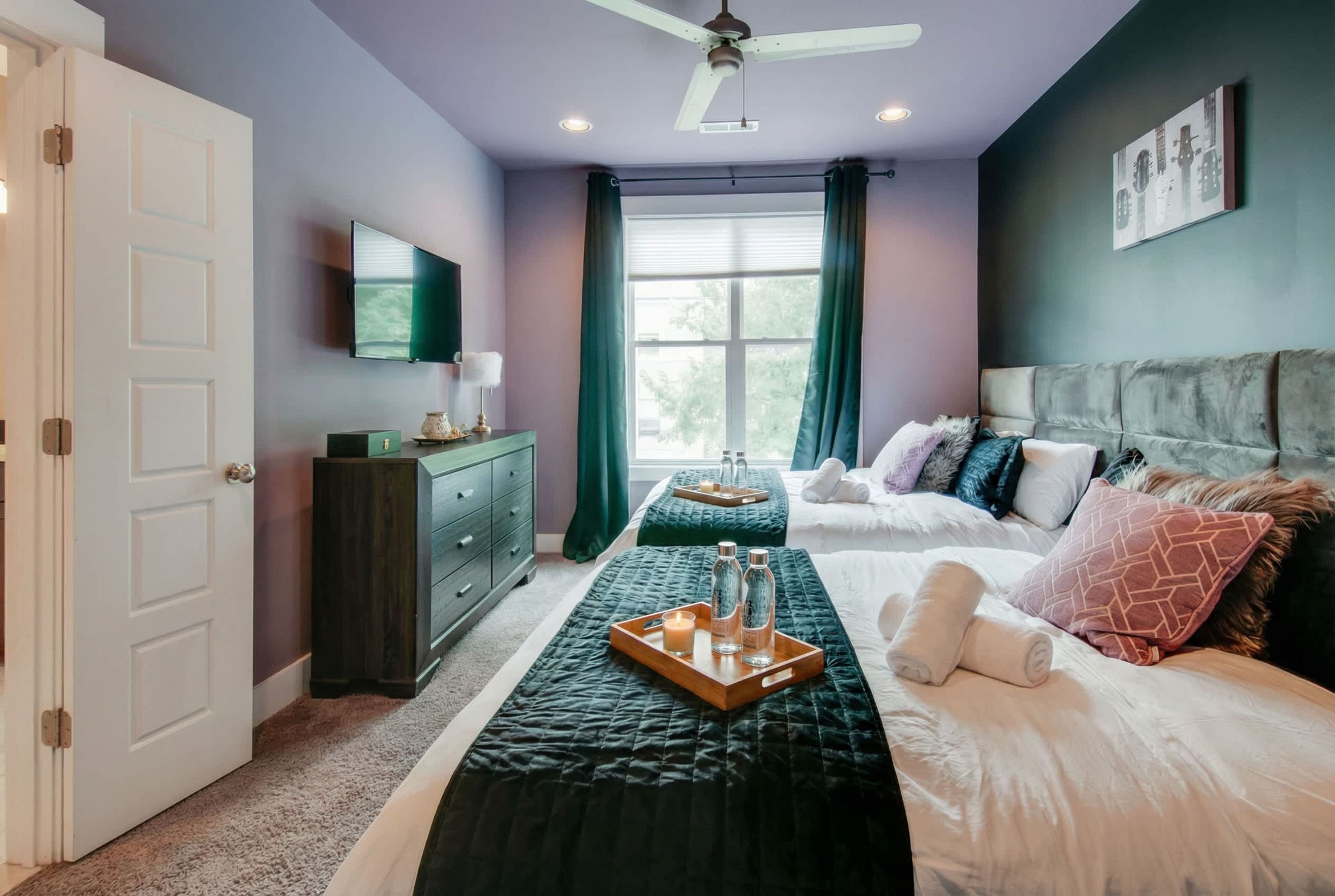 A bedroom with two beds, a ceiling fan, a TV, a dresser, and a window with curtains.