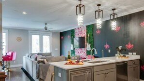 A modern kitchen with a central island, stainless steel appliances, and a decorative wall with floral and guitar motifs. - Close to the Gulch - Book Today (Nashville)