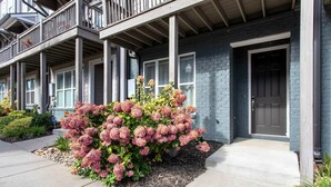Een woonhuis met een veranda, een deur en een tuin met roze bloemen.