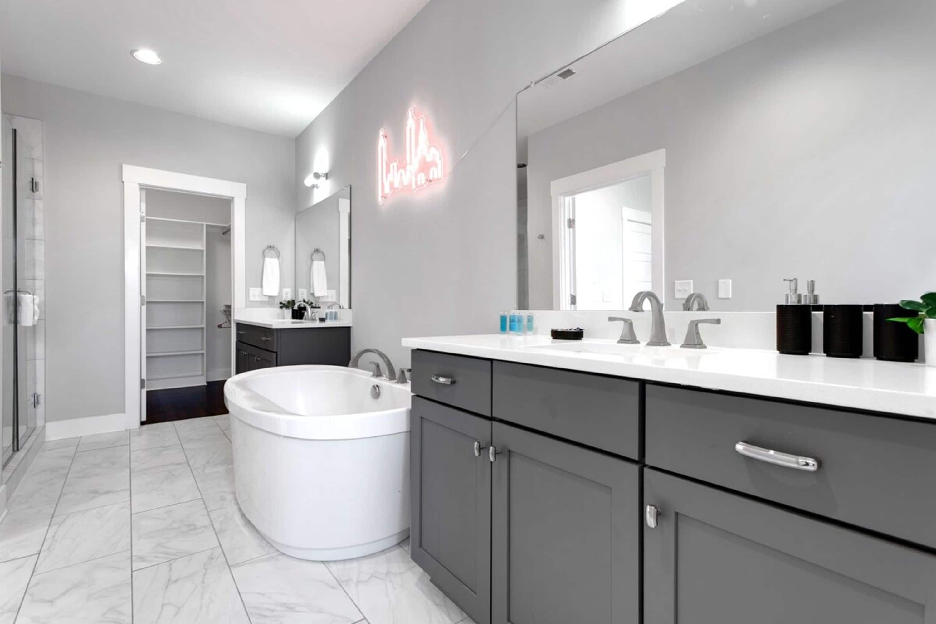 A modern bathroom with a large bathtub, a vanity with a mirror, and a neon sign.
