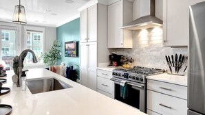 A modern kitchen with white cabinets, a stainless steel refrigerator, and a gas stove. - Near Gulch 12 South Book Luxury Now (Nashville)