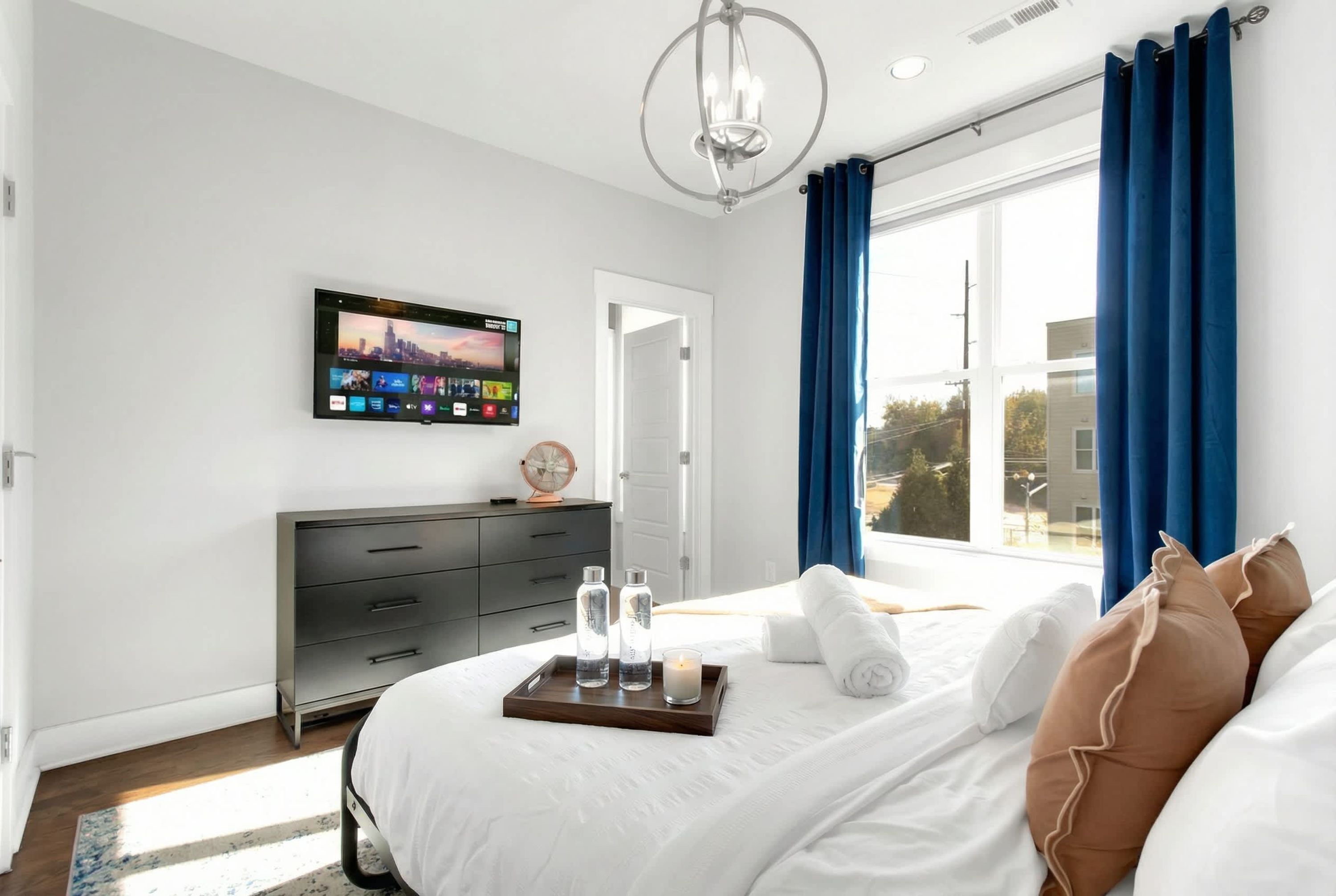 Una habitación de hotel moderna con una cama grande, un televisor de pantalla plana montado en la pared, un aparador y una ventana con cortinas azules.