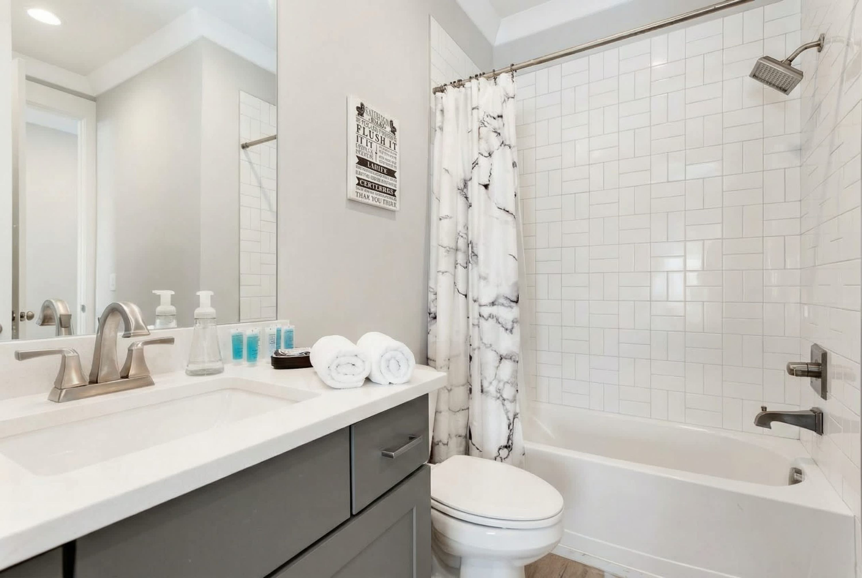 Un baño con lavamanos blanco, espejo y ducha con cortina de mármol.