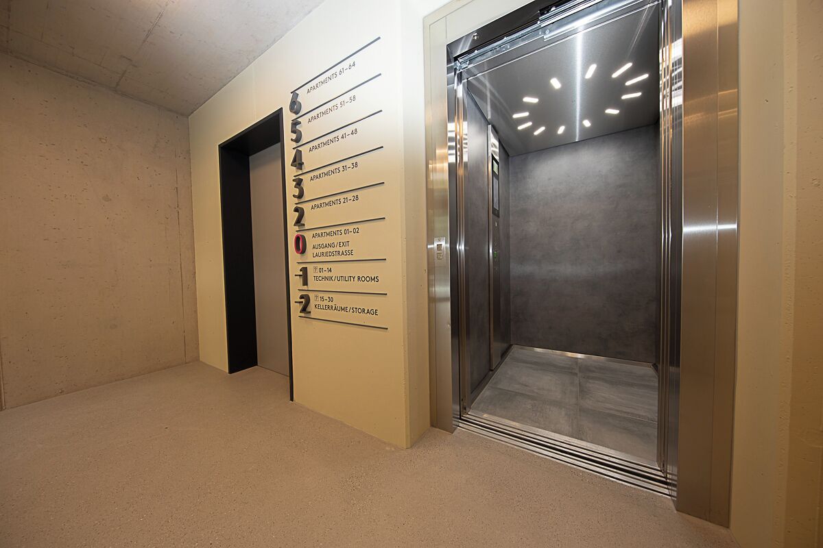 An elevator with a digital display and a wall with apartment numbers and room types.