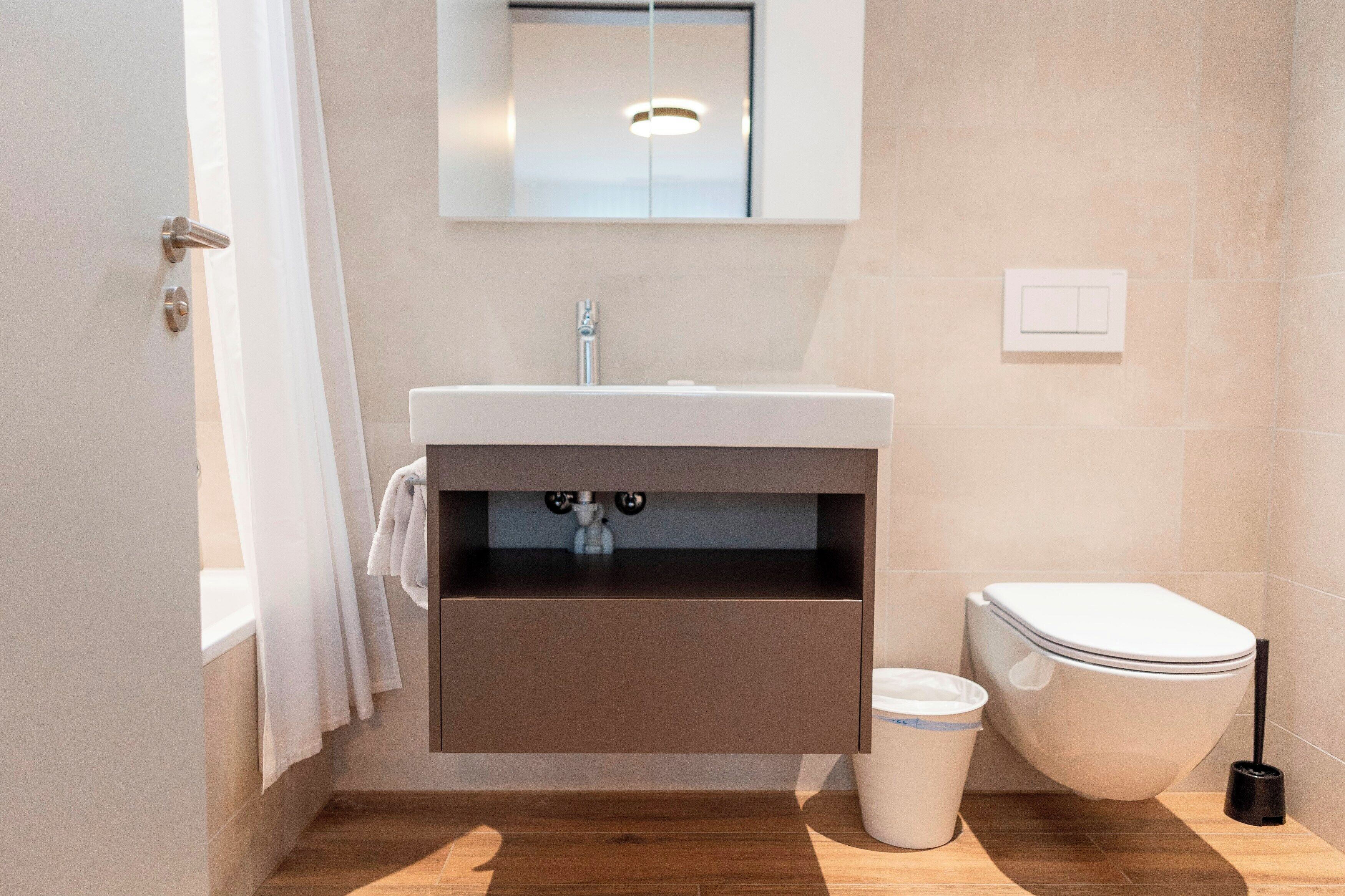 Un baño moderno con un lavamanos blanco, un inodoro y un cubo de basura.