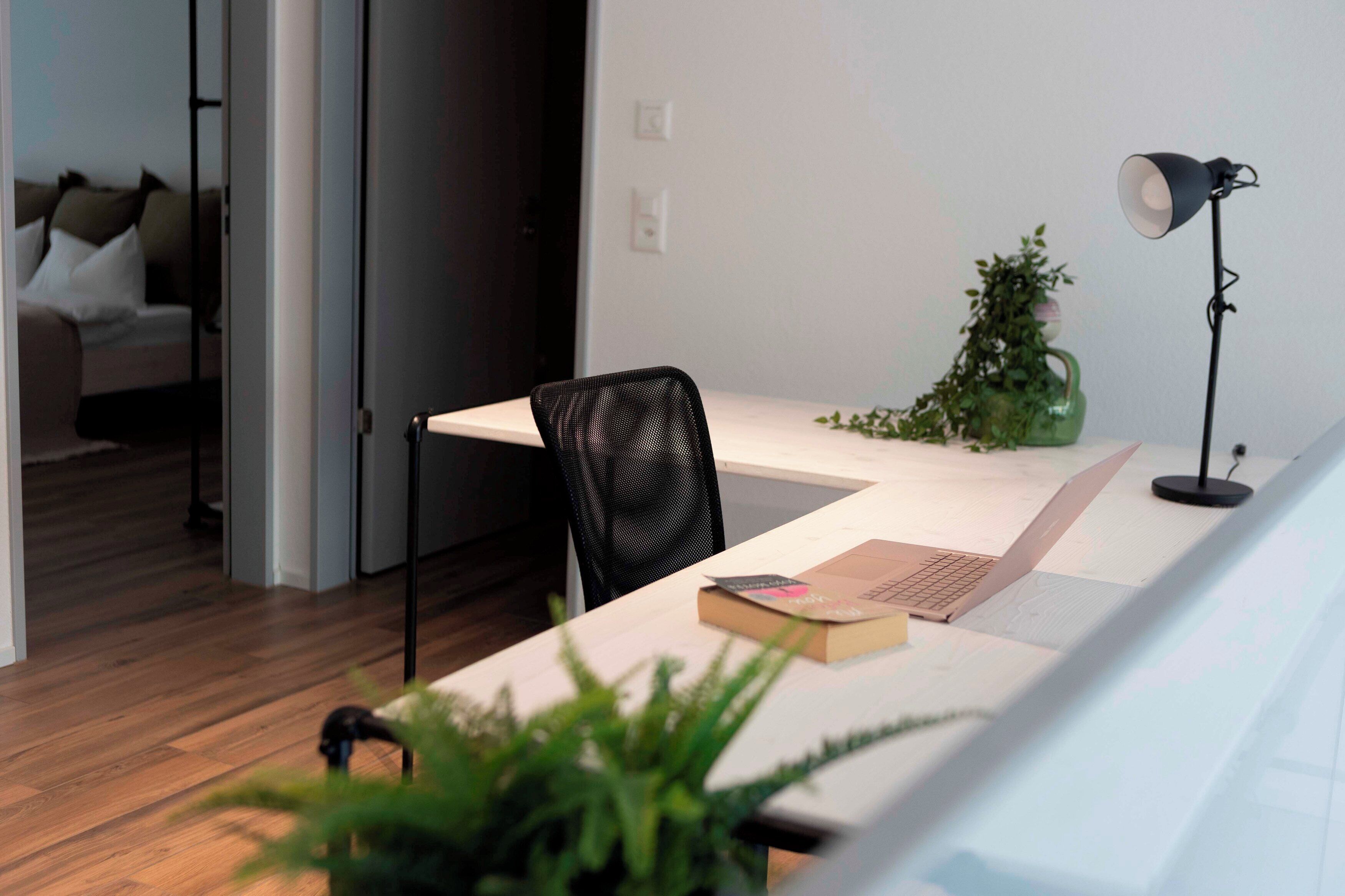 Un espacio de trabajo moderno con escritorio, silla, ordenador portátil, lámpara y una planta pequeña.