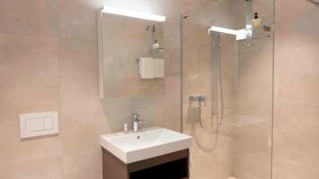 Een moderne badkamer met een glazen douchecabine, een wit wastafeltje en een spiegel.