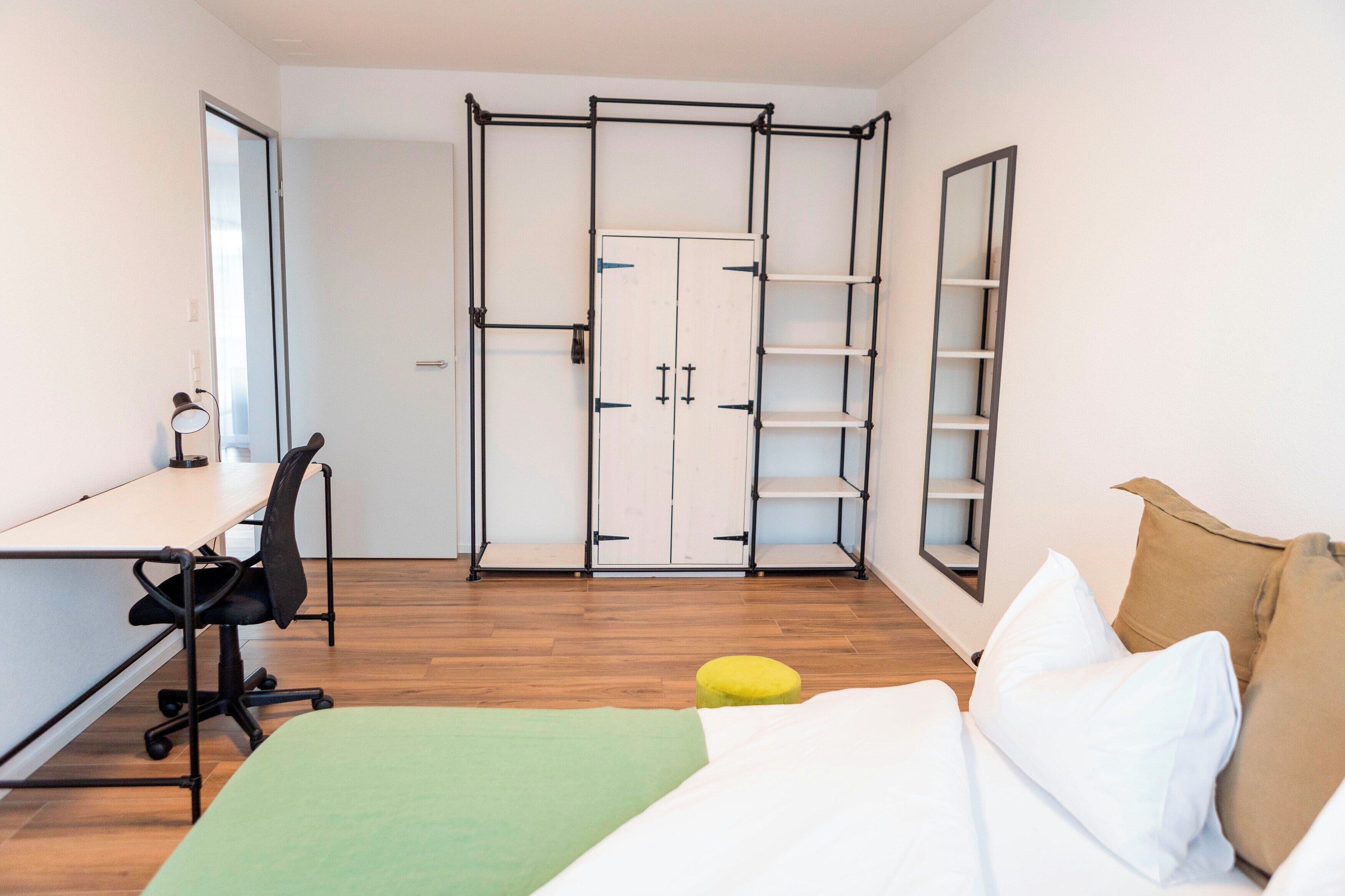 Un dormitorio con cama, escritorio, silla, armario y estantería.