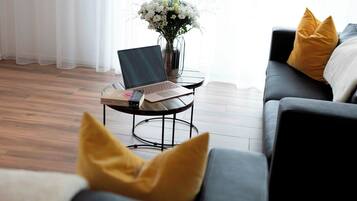 A modern living room with a laptop on a small round table, a vase with flowers, and a sofa with cushions.