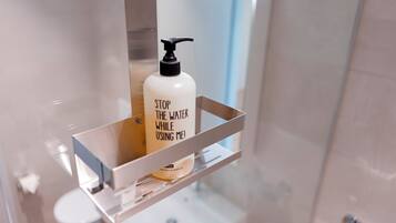 A bathroom with a white bottle of shampoo on a shelf and a mirror above it.