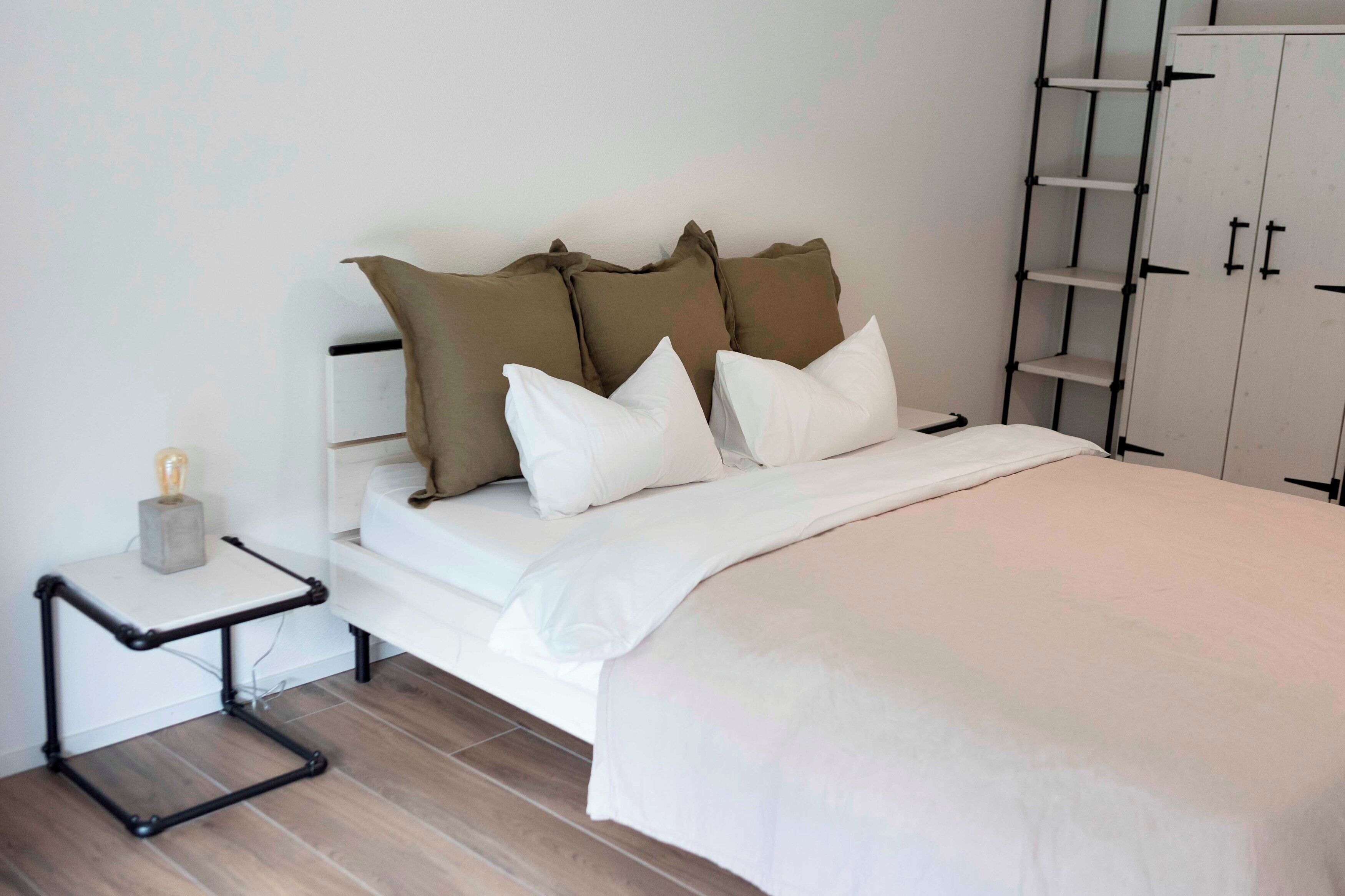 A neatly arranged bedroom with a bed, pillows, a bedside table, and a wardrobe.