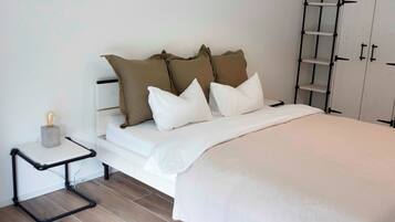 A neatly arranged bedroom with a bed, pillows, a bedside table, and a wardrobe.