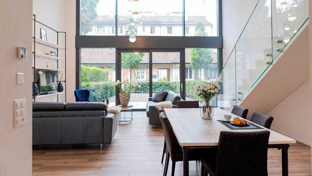 A modern dining area with a large table, chairs, and a view of the outdoors through large windows. - THE CITY ZUG APARTMENTS (Zug)