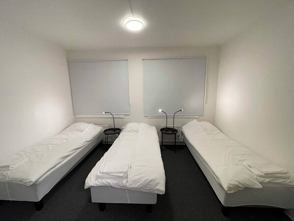A room with three single beds, a small table between each bed, and a ceiling light. - Office Motel (Gothenburg)