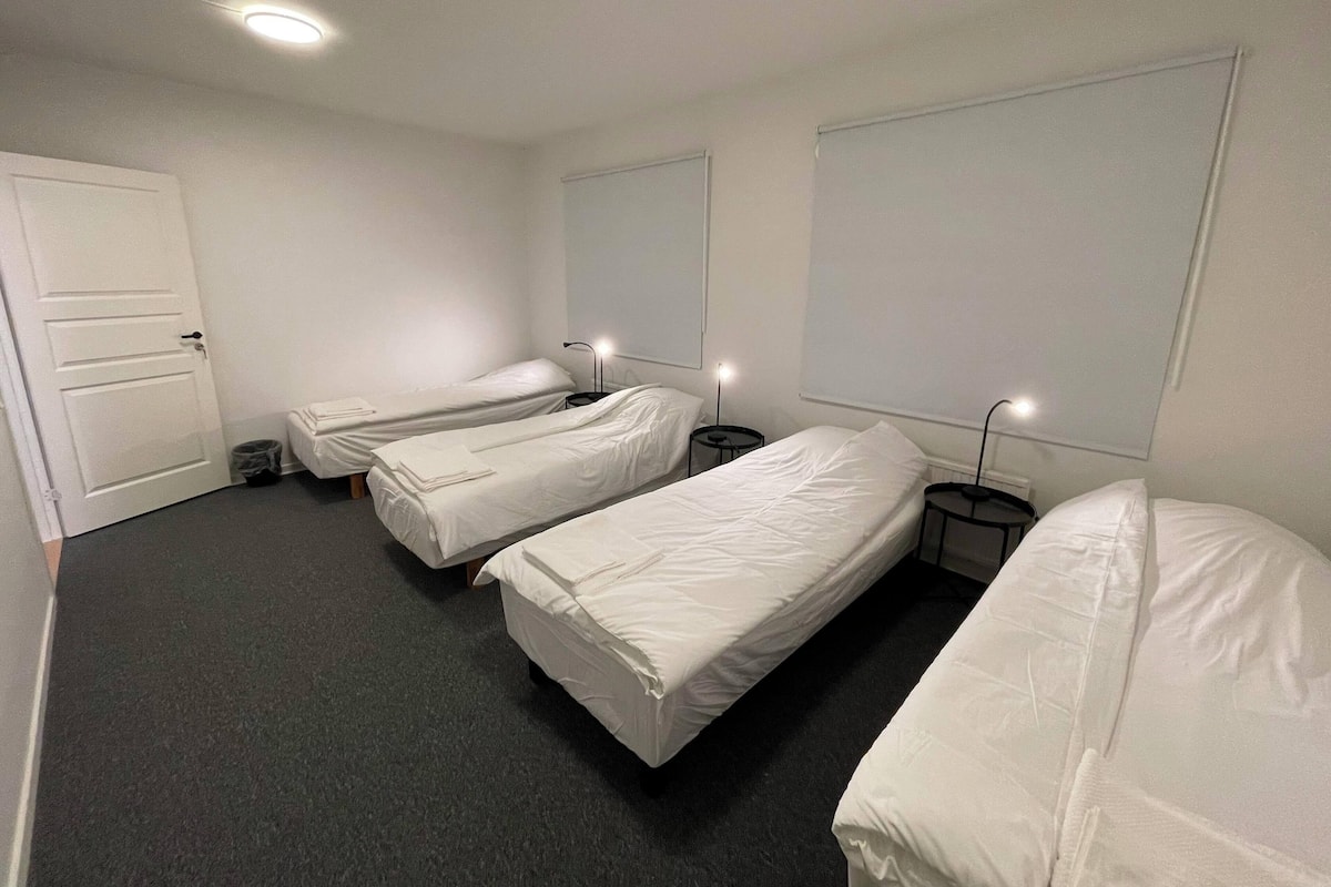 Ein Hotelzimmer mit drei Einzelbetten, einer Tür, einem Mülleimer und einem Fenster.