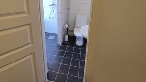 A bathroom with a white toilet, a shower area, and a tiled floor. - Office Motel (Gothenburg)