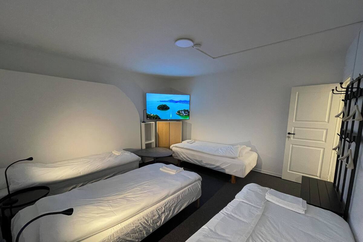 Ein Hotelzimmer mit zwei Einzelbetten, einem kleinen Tisch, einem an der Wand befestigten Fernseher und einer Tür mit Kleiderhaken.