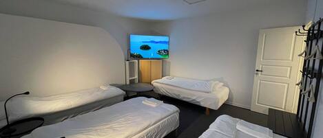 A hotel room with two single beds, a small table, a TV on the wall, and a door with coat hooks.