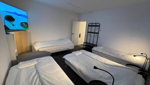 A hotel room with three single beds, a TV mounted on the wall, a wardrobe, and a coat rack. - Office Motel (Gothenburg)