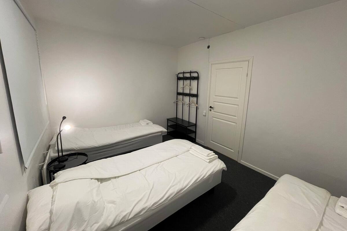Ein kleines, sauberes Zimmer mit zwei Einzelbetten, einem Nachttisch, einer Lampe und einem Kleiderhaken.