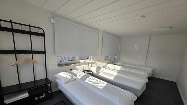 A hotel room with two beds, a bedside table, a hanging rack, and a window with blinds. - Office Motel (Gothenburg)