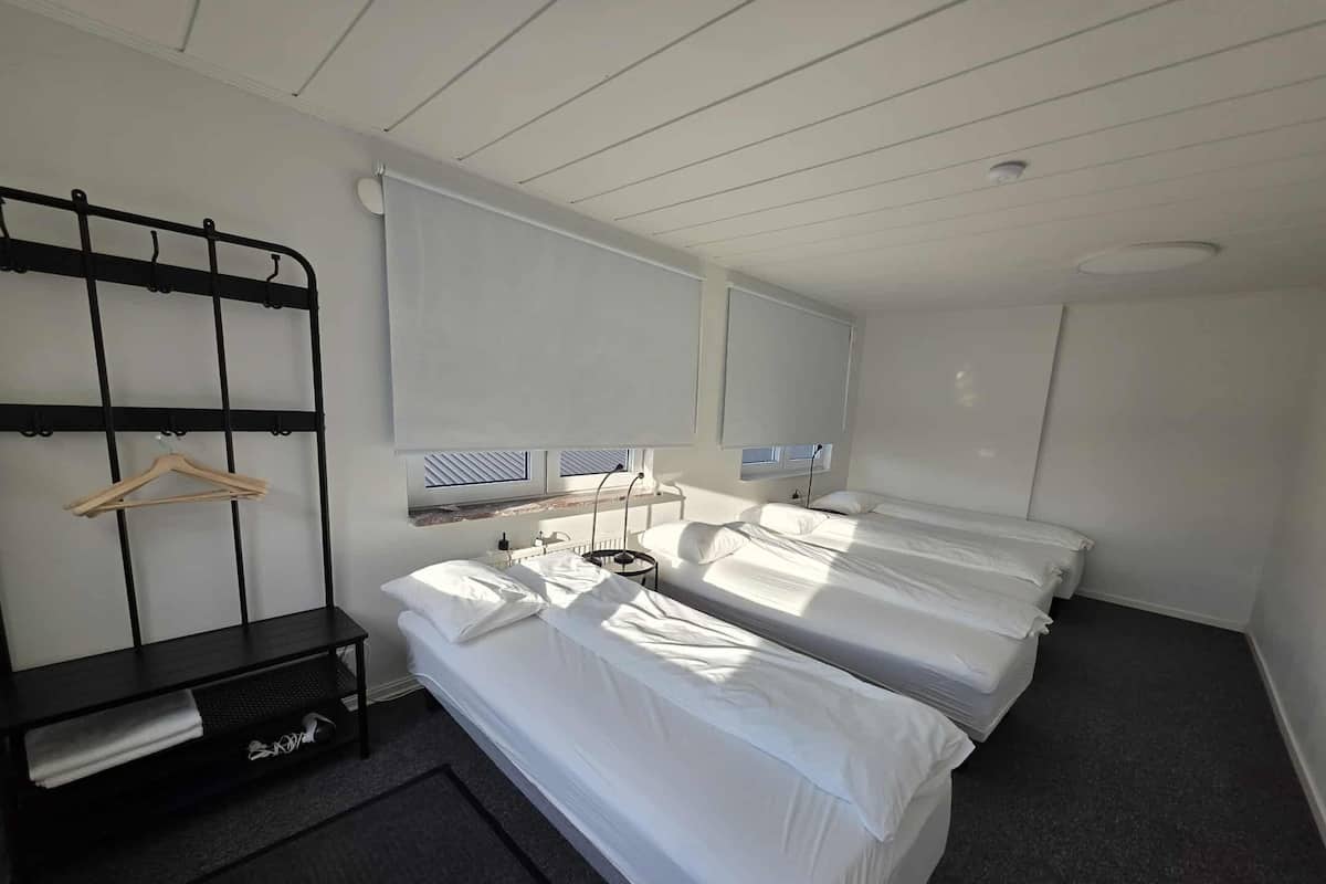Ein Hotelzimmer mit zwei Betten, einem Nachttisch, einer Kleiderstange und einem Fenster mit Jalousien.