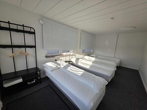 A hotel room with two beds, a bedside table, a hanging rack, and a window with blinds. - Office Motel (Gothenburg)